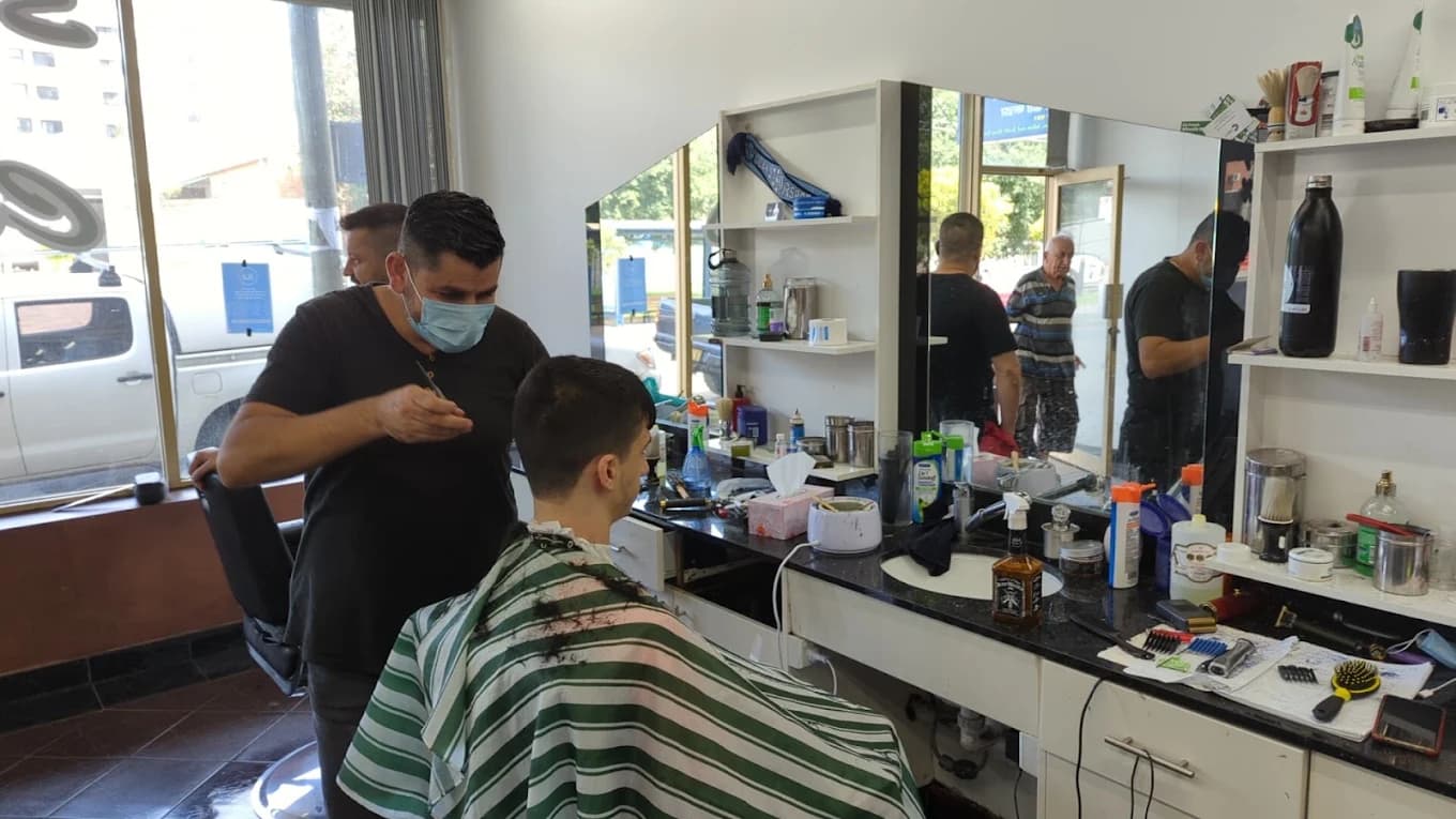 A barber cutting a customer's hair inside Style N Cuts Auburn, with the shop's mirrors and workstations visible